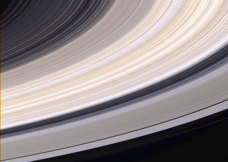 Una vista de cerca de los anillos de Saturno. Son grises y tostados, y hay espacios intermedios donde puedes ver el color negro del espacio a través de ellos.