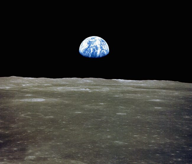 View across lunar landscape, with distant Earth, top half lit, rising above the horizon.